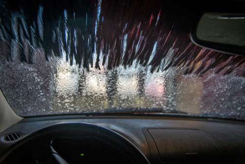 Inifrån en bil när en ruta tvättas i en biltvätt